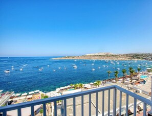 A coastal view with boats, a beach, and a pool area.