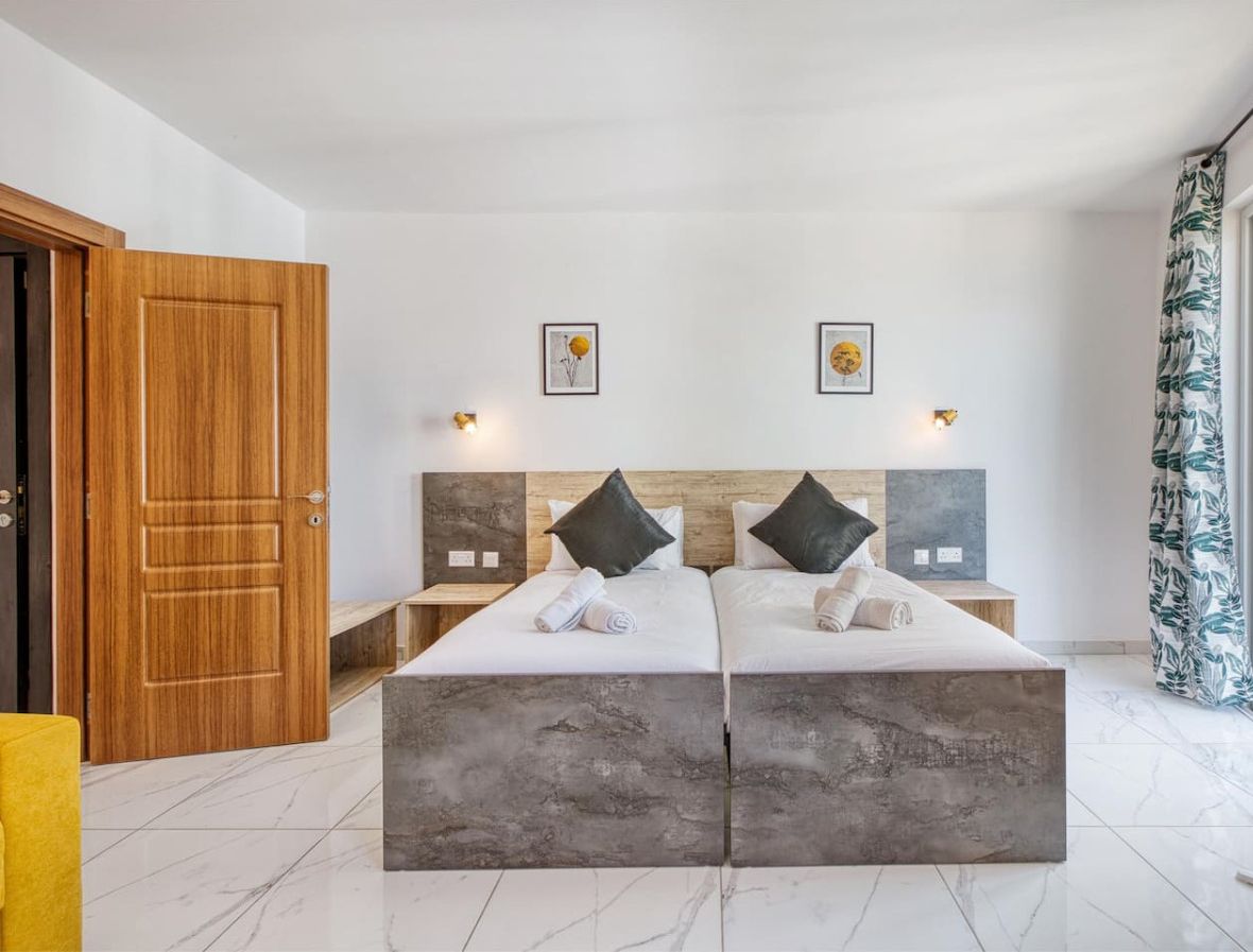 Een moderne slaapkamer met een groot bed, twee nachtkastjes, een houten deur en een raam met gordijnen.