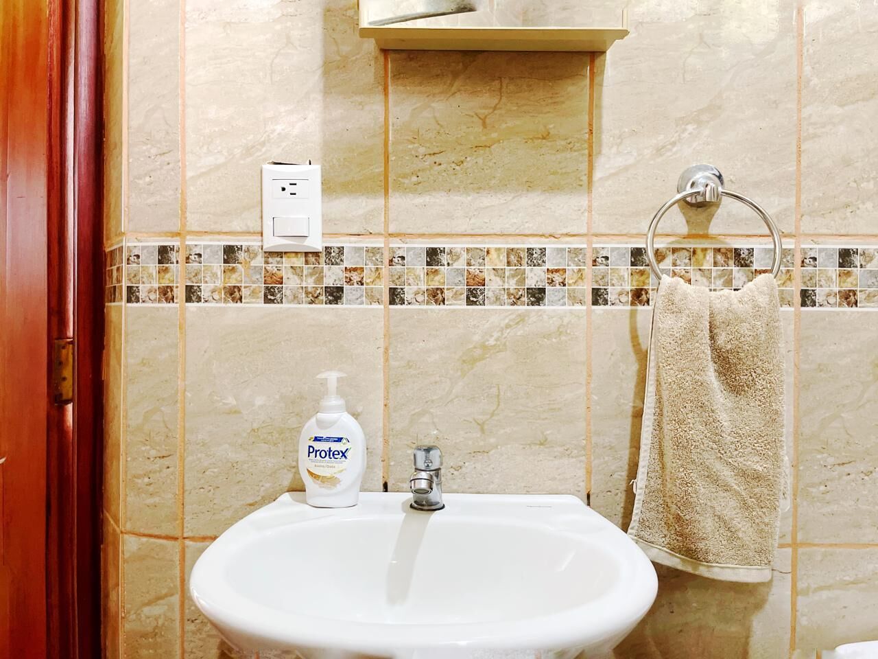 Un bagno con lavandino, sapone liquido, asciugamano e interruttore della luce a parete.