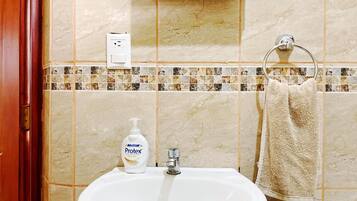Un bagno con lavandino, sapone liquido, asciugamano e interruttore della luce a parete.