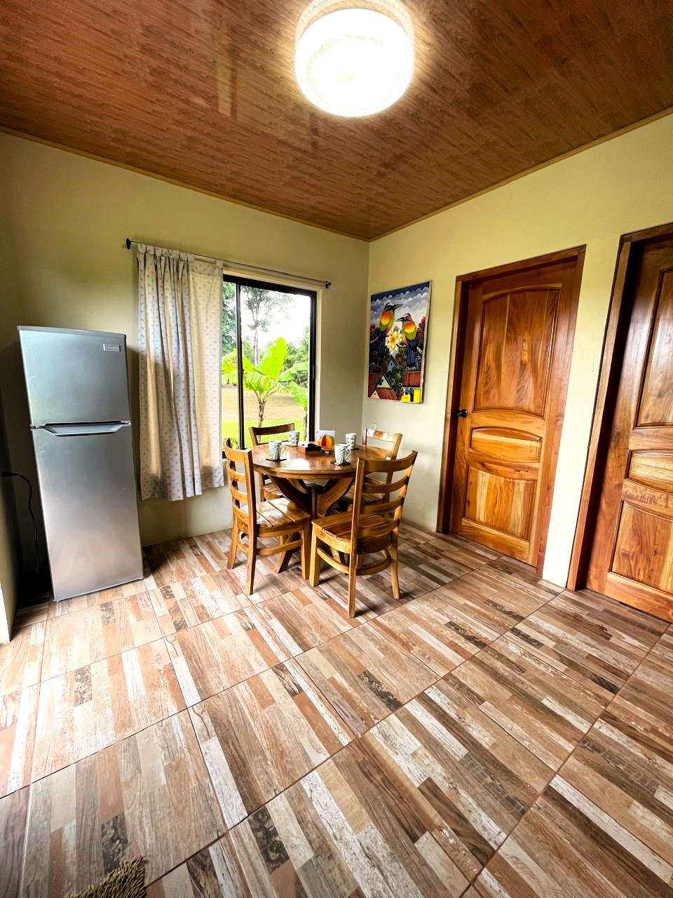 A compact kitchen with a refrigerator, a dining table with chairs, and a window with curtains.