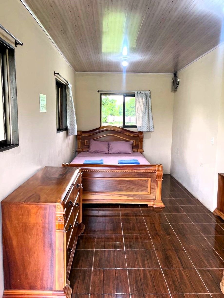Een slaapkamer met een houten bed, een houten dressoir en een raam met gordijnen.