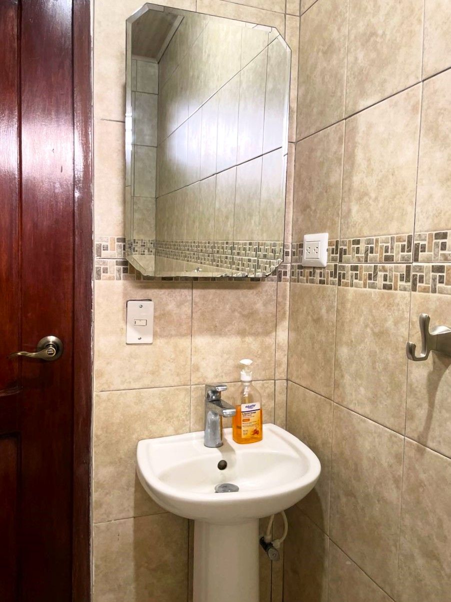 Un bany amb un lavabo blanc, un mirall i una porta de fusta.