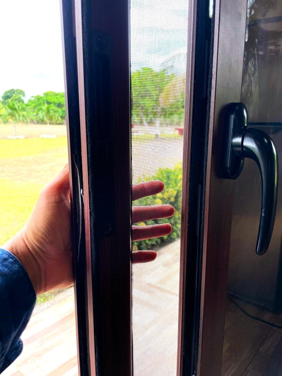 A hand holding a door with a metal handle and a mesh screen.