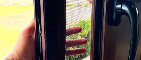 A hand holding a door with a metal handle and a mesh screen.