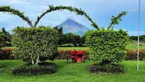 Un jardín ajardinado con un banco rojo, arbustos bien cuidados y una montaña al fondo.