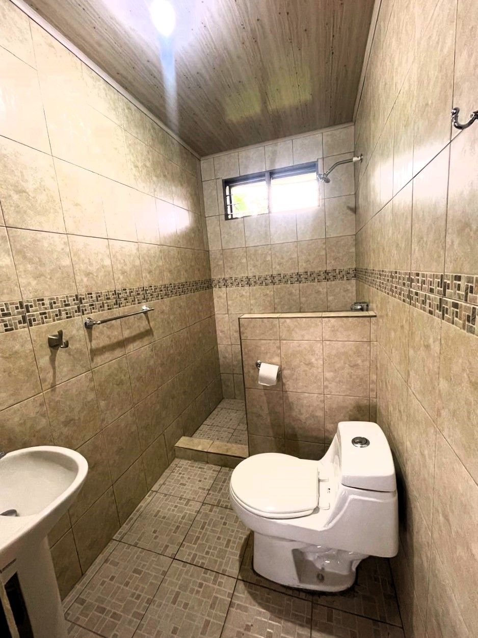 A small, tiled bathroom with a toilet, sink, and shower area.