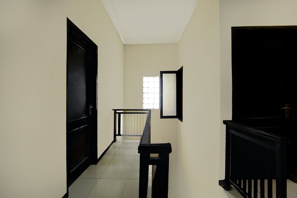Un pasillo con una puerta negra a la izquierda, una ventana con persianas y un banco negro en el centro.