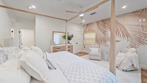 A modern bedroom with a large bed, a vanity with a mirror, a chair, and a ceiling fan.