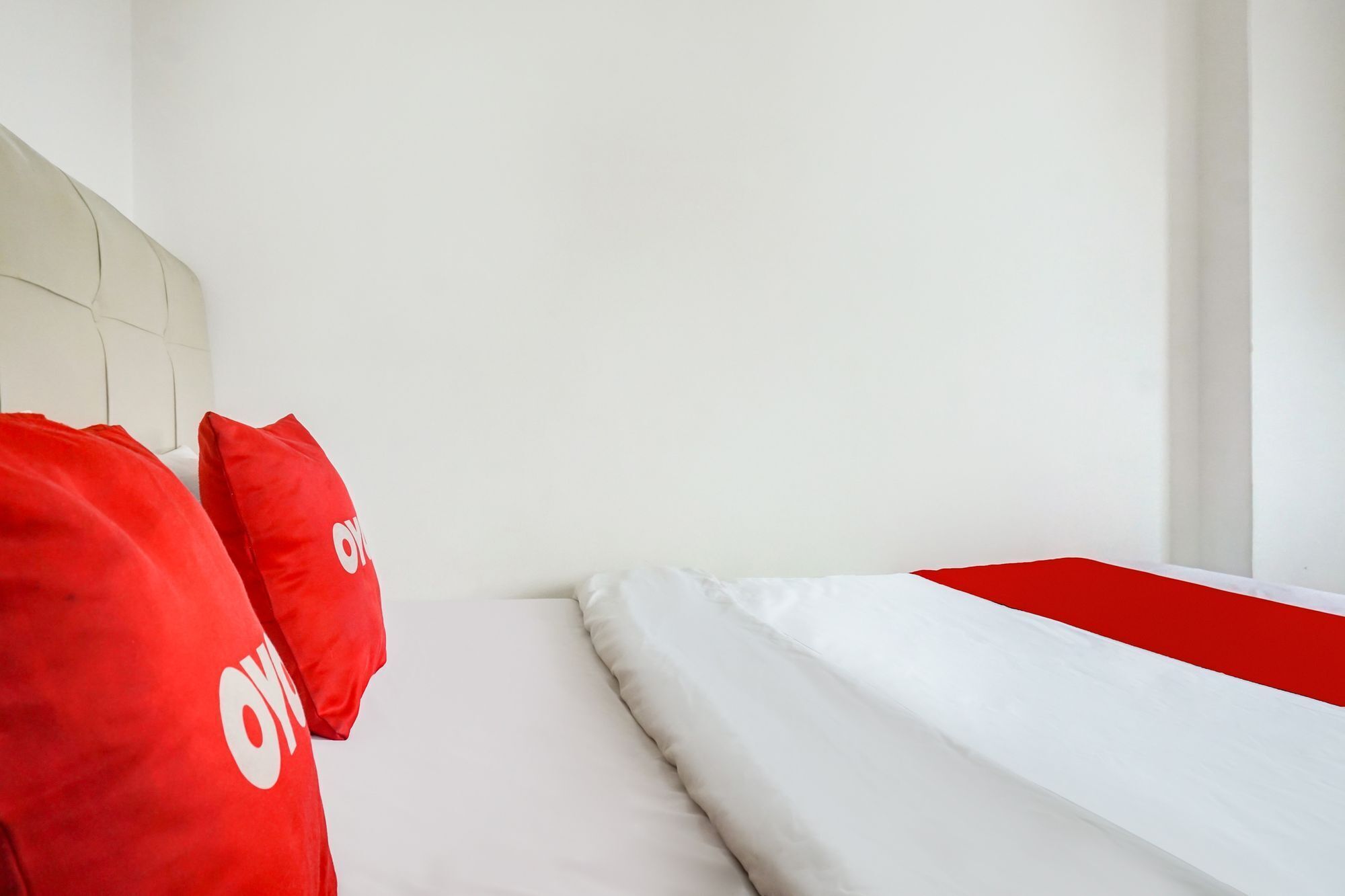 A hotel room with a white headboard, a bed with white and red bedding, and red pillows with a logo.