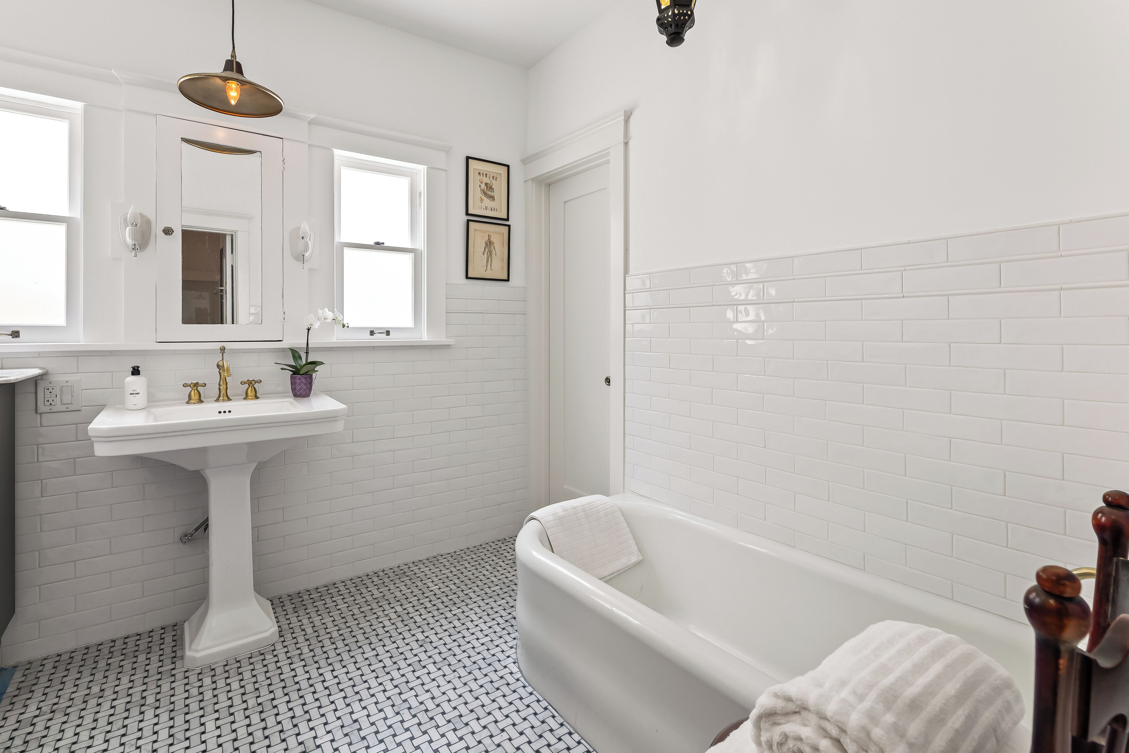 A bathroom with a white pedestal sink, a bathtub, and a window.