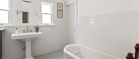 A bathroom with a white pedestal sink, a bathtub, and a window.