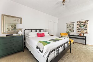 A neatly arranged bedroom with a bed, bedside tables, a desk, and artwork on the walls.