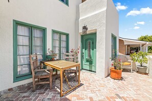 Eine Terrasse mit einem Holztisch und Stühlen, einer grünen Tür und Blumentöpfen.