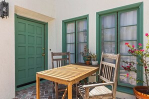A wooden table and chairs outside a building with green-framed windows and a green door.