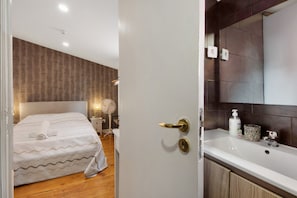 A hotel room with a bed, bedside table, lamp, and a bathroom with a sink and mirror.