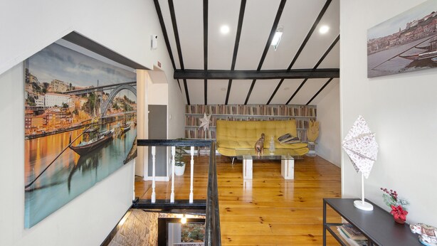 Um quarto com piso de madeira, escada, sofá, mesa e um quadro de uma ponte.