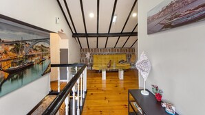 Um amplo loft com teto alto, vigas de madeira, escada, sofá, estante de livros e um quadro de uma ponte.