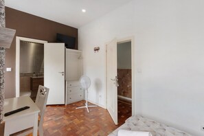 Un dormitorio con cama, escritorio, silla, ventilador y armario.