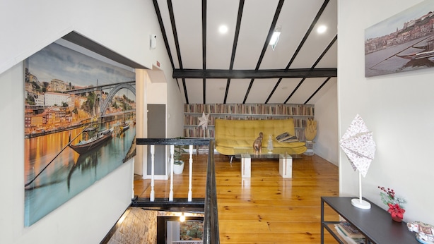 Um quarto com piso de madeira, escada, sofá, mesa e um quadro de uma ponte.