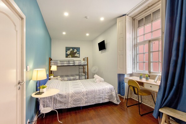 A room with a bunk bed, a desk with a chair, a window with curtains, a wall-mounted TV, and a fan.