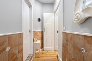 A narrow hallway with a wooden floor, a white door, and a small table with a bottle and a cup.