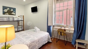 Ein Schlafzimmer mit Etagenbett, Schreibtisch, Stuhl, Fernseher und einem Fenster mit Vorhängen.