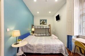 A bedroom with a bunk bed, a desk, a chair, a lamp, and a painting on the wall.