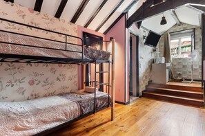 A bunk bed room with a wooden floor, a desk with a chair, and a television.