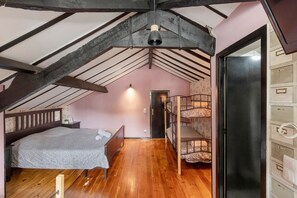 A bedroom with a wooden floor, a bunk bed, a single bed, a ceiling fan, and a door leading to another room.