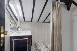 Un baño con lavamanos blanco, azulejos estampados, una viga de techo negra y cortina de ducha color beige.