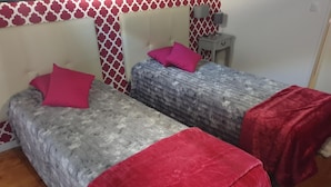 A room with two beds, each with a red pillow and blanket, against a wall with a red and white pattern.