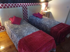 Une chambre avec deux lits, chacun agrémenté d’un oreiller et d’une couverture rouges, et un mur orné de motifs.