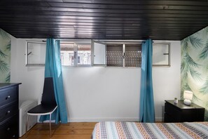 Een slaapkamer met een bed, een stoel, een bureau, een raam met gordijnen en een muur met een bladmotief.