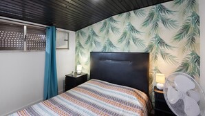 A bedroom with a bed, a nightstand, a lamp, a fan, and a window with a curtain. - Room 'K' with Shared Garden and Wi-Fi (Porto)