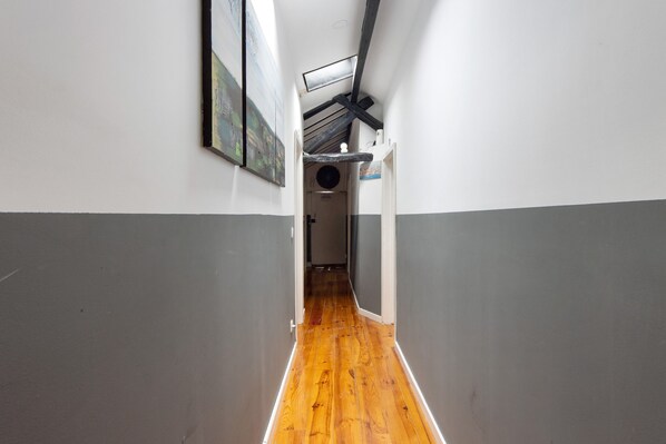 A narrow hallway with wooden flooring, white and gray walls, and a ceiling with exposed beams.