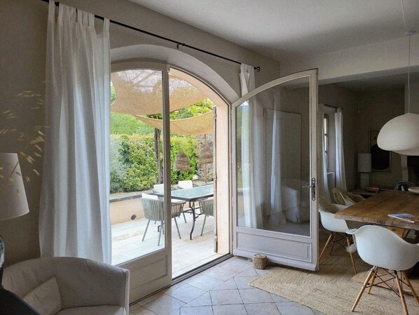 A room with a sliding glass door leading to an outdoor patio, a dining table with chairs, a sofa, and a lamp.