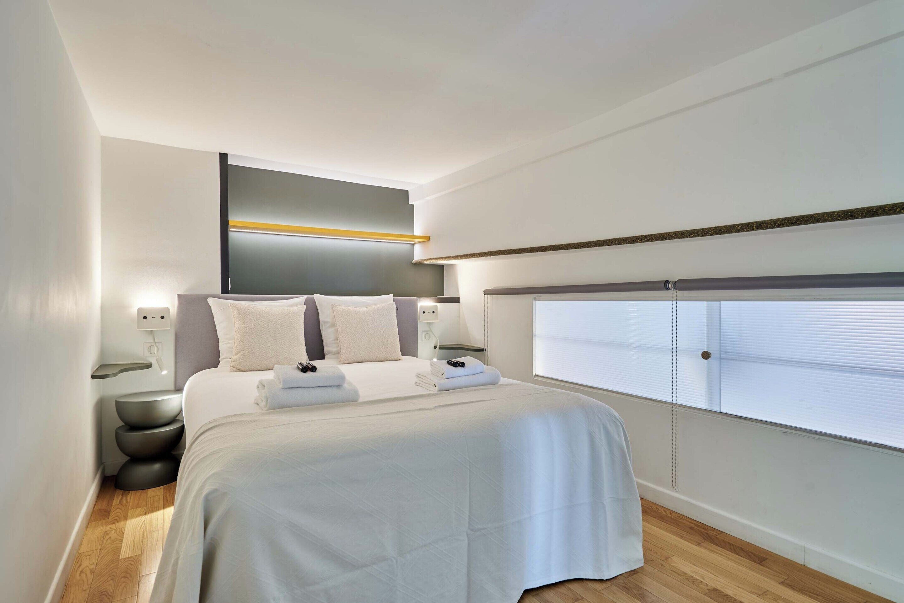 A modern hotel room with a large bed, bedside tables, a built-in bench, and a view of the city.
