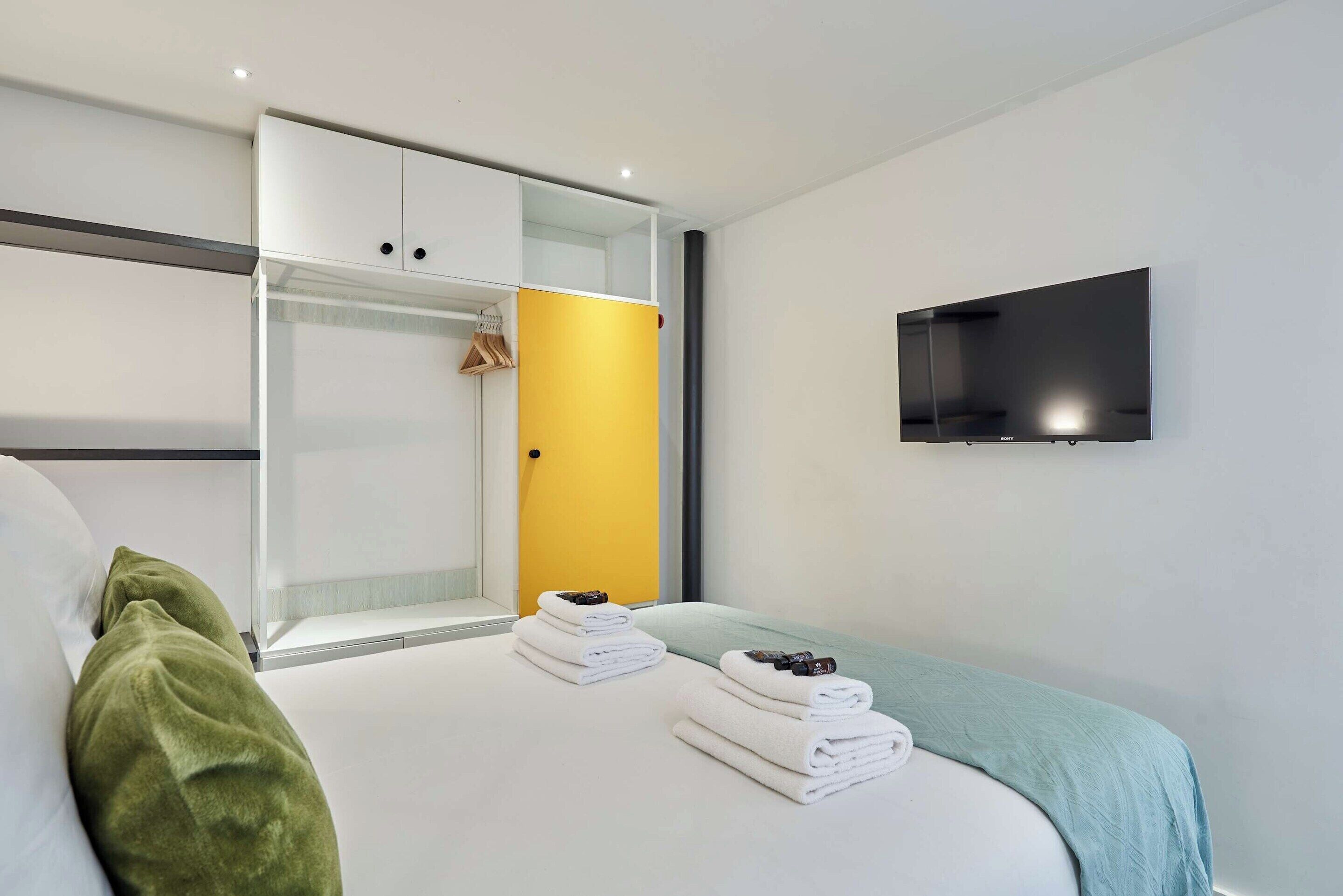 Ein modernes Hotelzimmer mit Bett, Wandfernseher und Kleiderschrank mit Glastür.