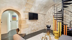 Un interior moderno con una pared de piedra, una escalera espiral negra y un televisor de pantalla plana montado en la pared.