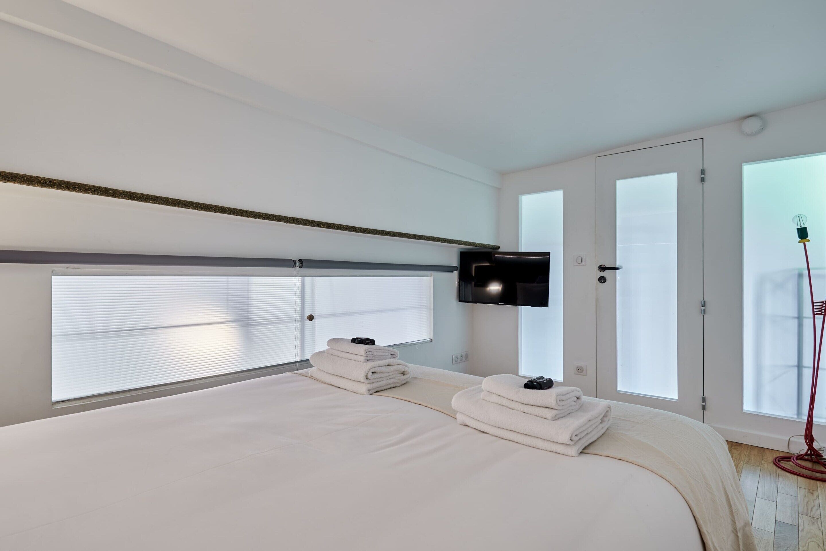 Une chambre d’hôtel moderne dotée d’un grand lit, d’un téléviseur à écran plat fixé au mur et d’une fenêtre avec des stores.