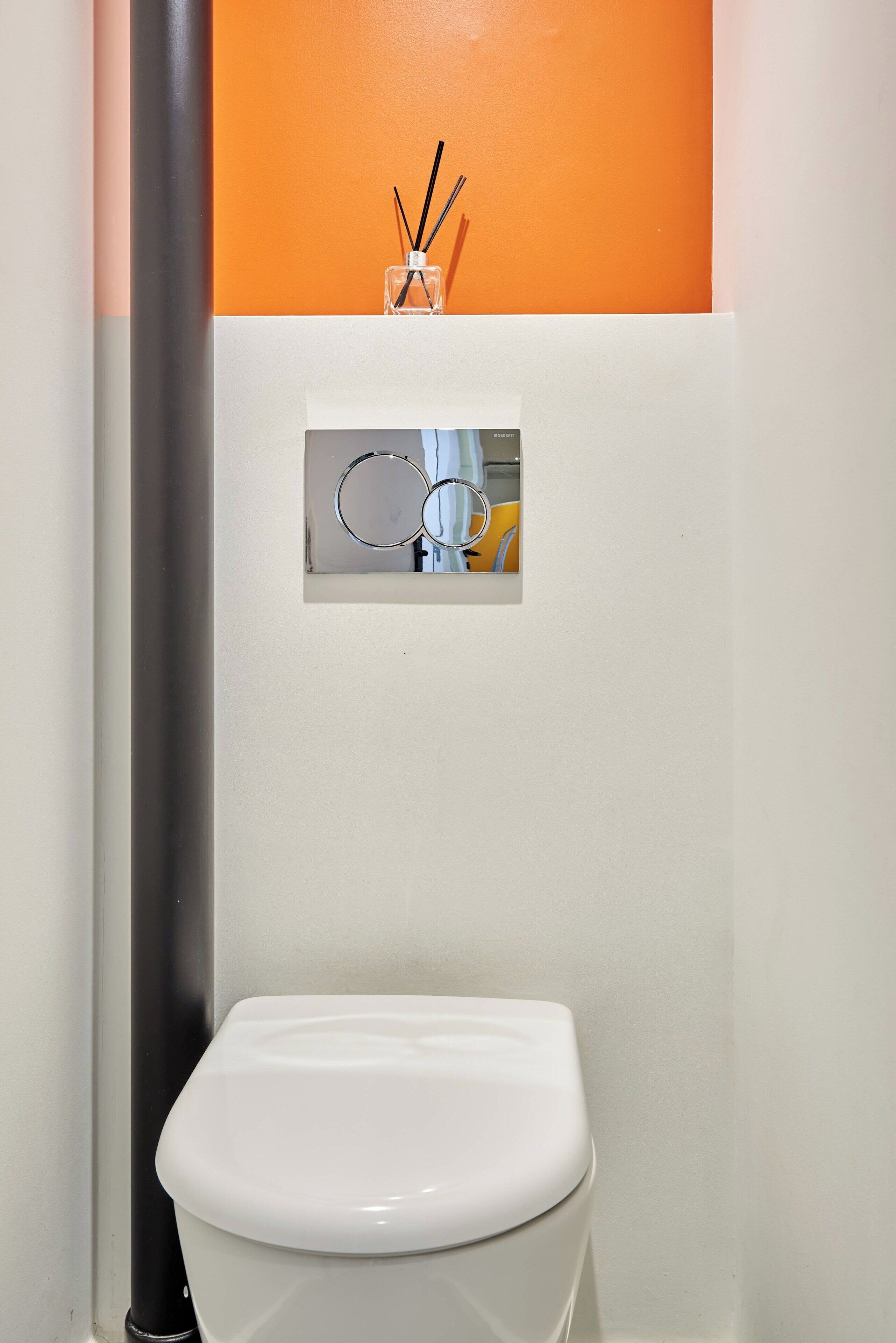 A bathroom with a white toilet, a black pipe, and a small window with a mirror and a glass container.