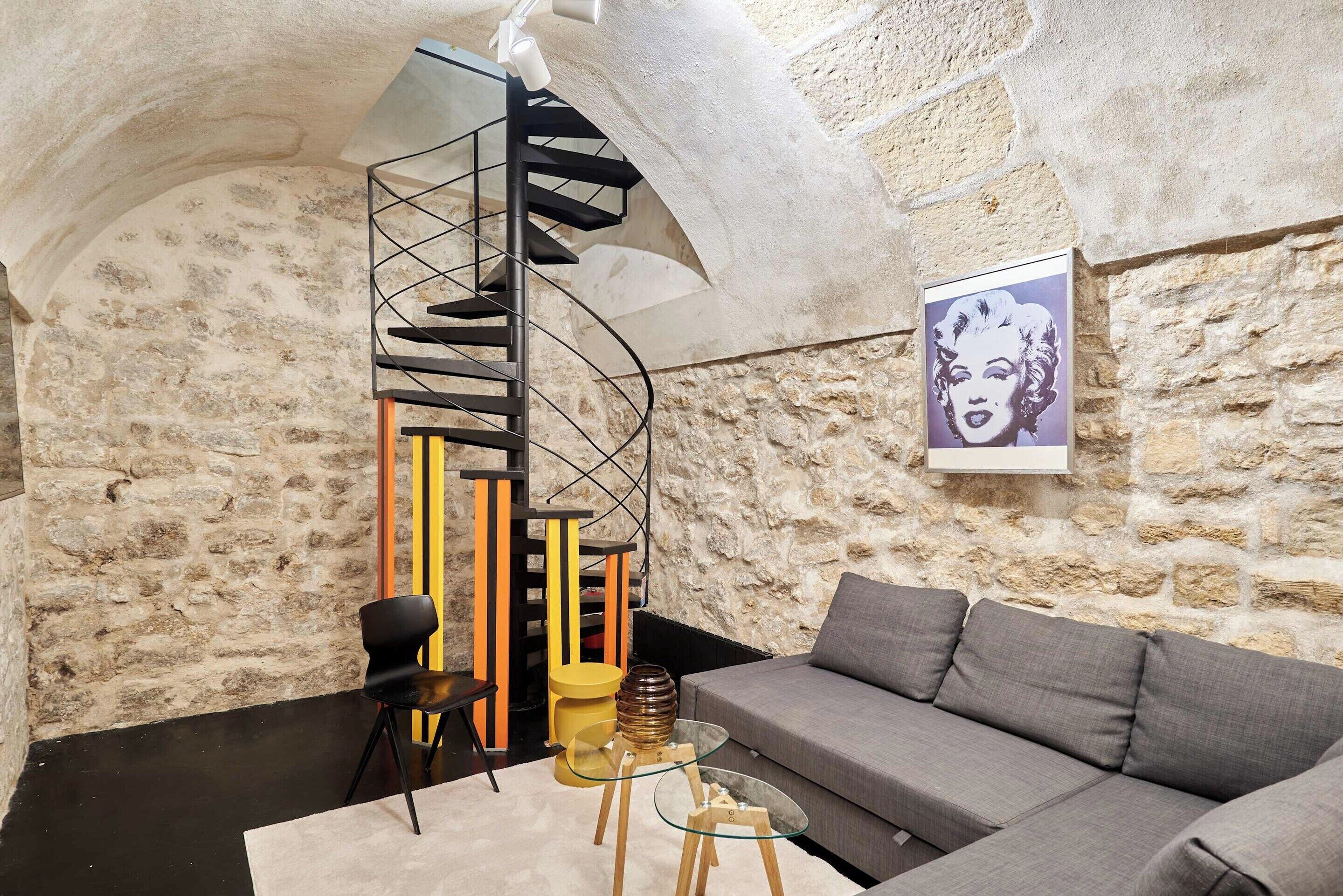 A modern interior with a spiral staircase, a sofa, a glass coffee table, and a stone wall.