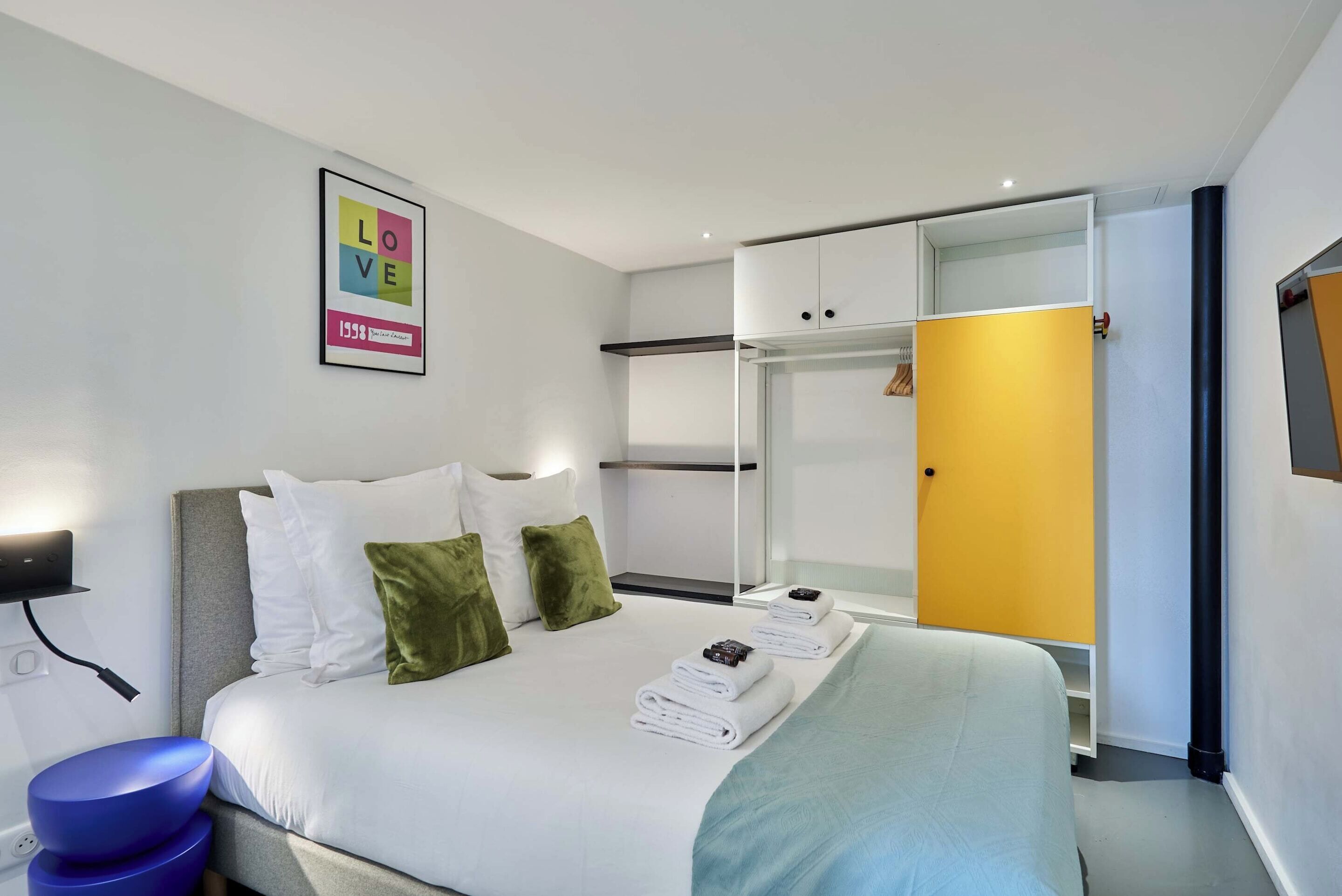 Una habitación de hotel moderna con cama, armario, espejo y un cartel enmarcado que dice 'LOVE'.