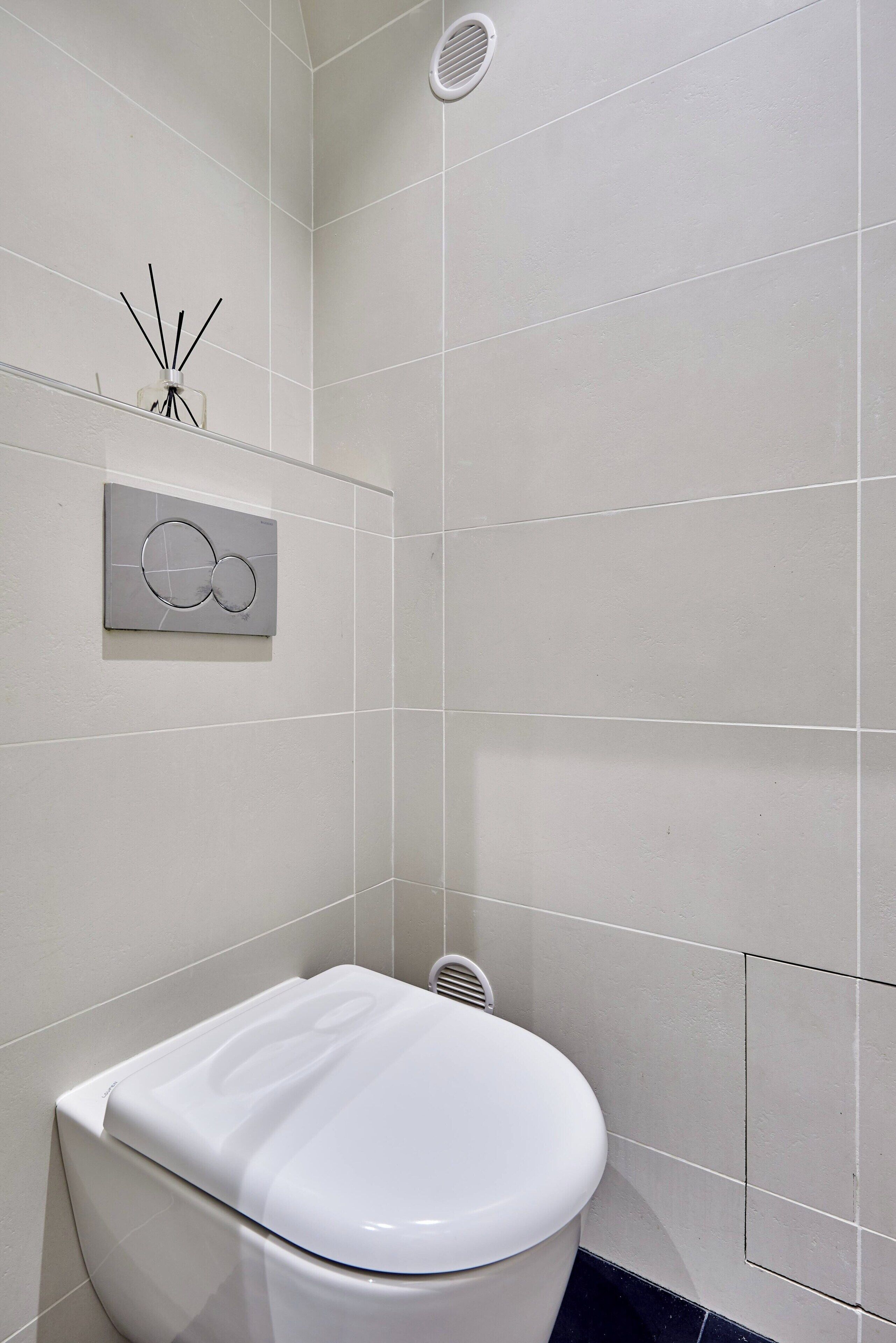 A bathroom with a toilet, a wall-mounted diffuser, and a vent.