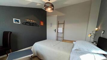 Une chambre d’hôtel avec un lit, une chaise, un porte-manteau, une échelle et un bureau avec une lampe.
