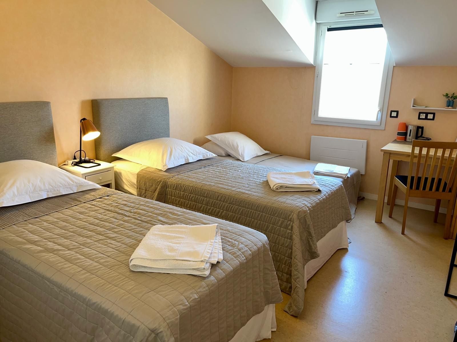 Et hotelværelse med to senge, et skrivebord og en stol.