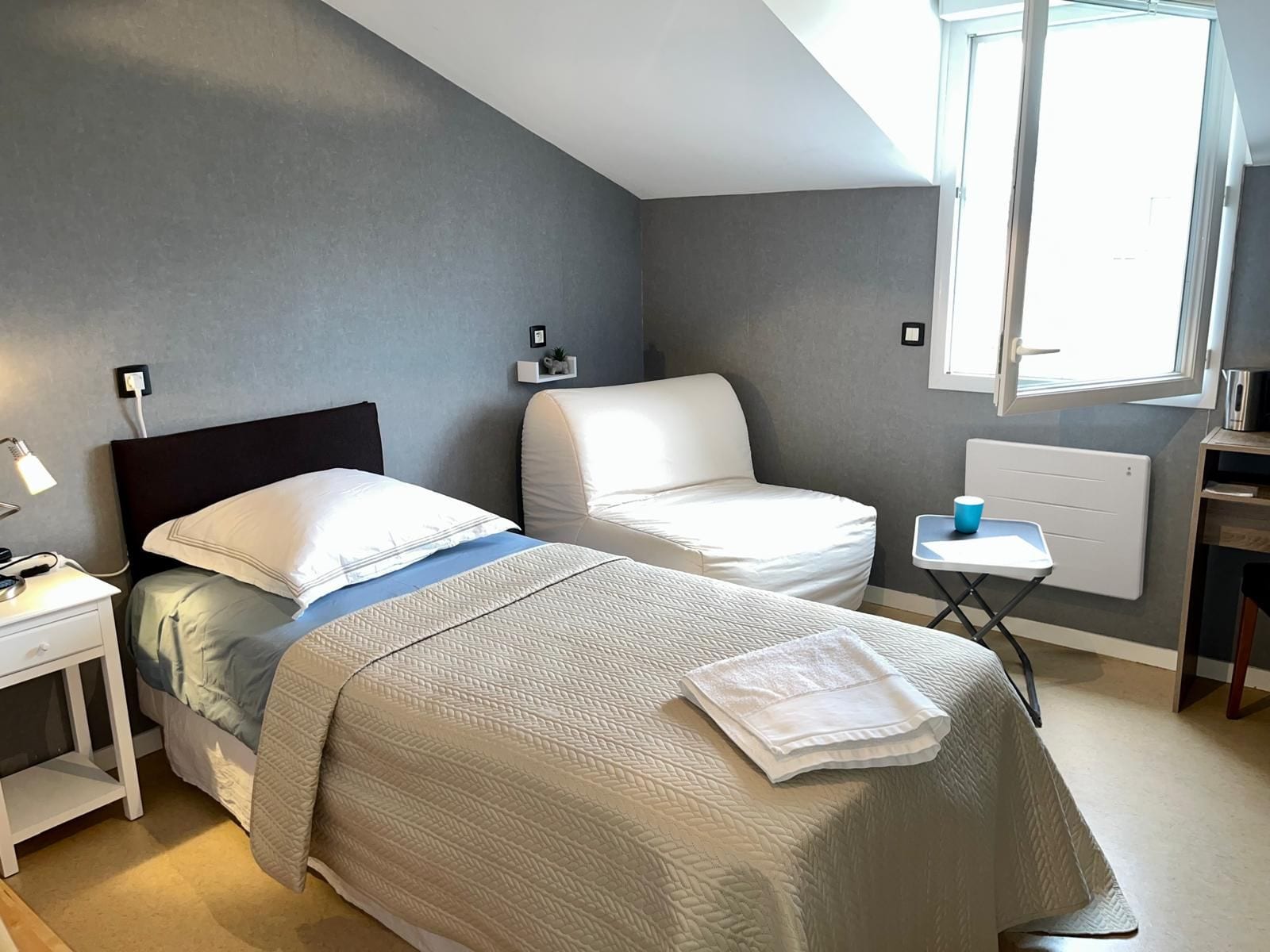 Un dormitorio con cama, mesita de noche, lámpara y ventana.