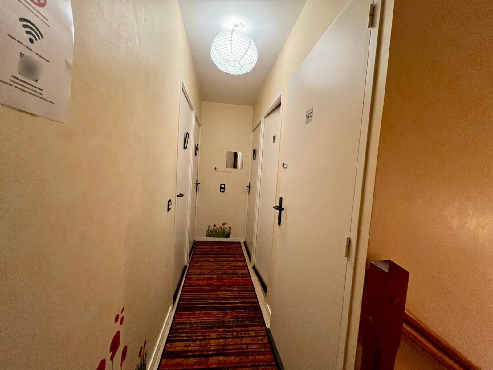 A narrow hallway with doors on both sides, a carpeted floor, and a light fixture on the ceiling.