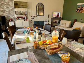 Un comedor con una mesa preparada para el desayuno, que incluye frutas, pan y bebidas.